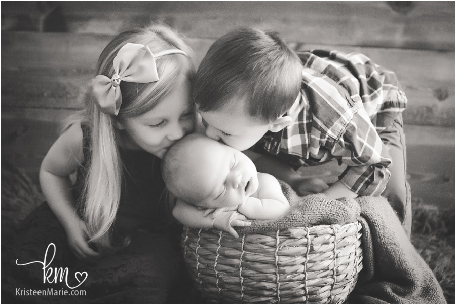 siblings kissing newborn brother in basket