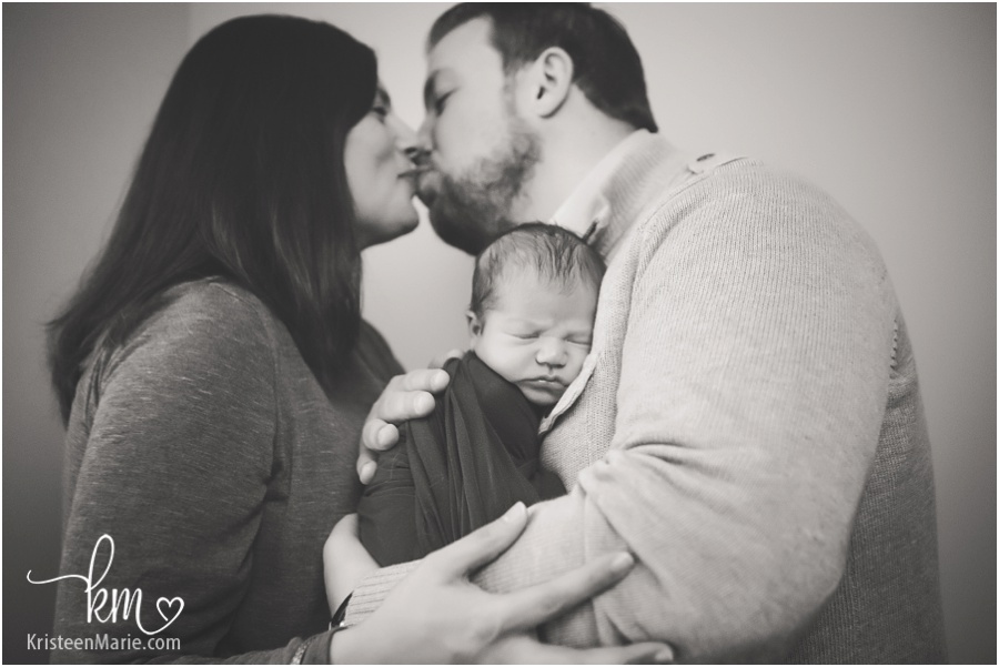 parents kissing with newborn baby