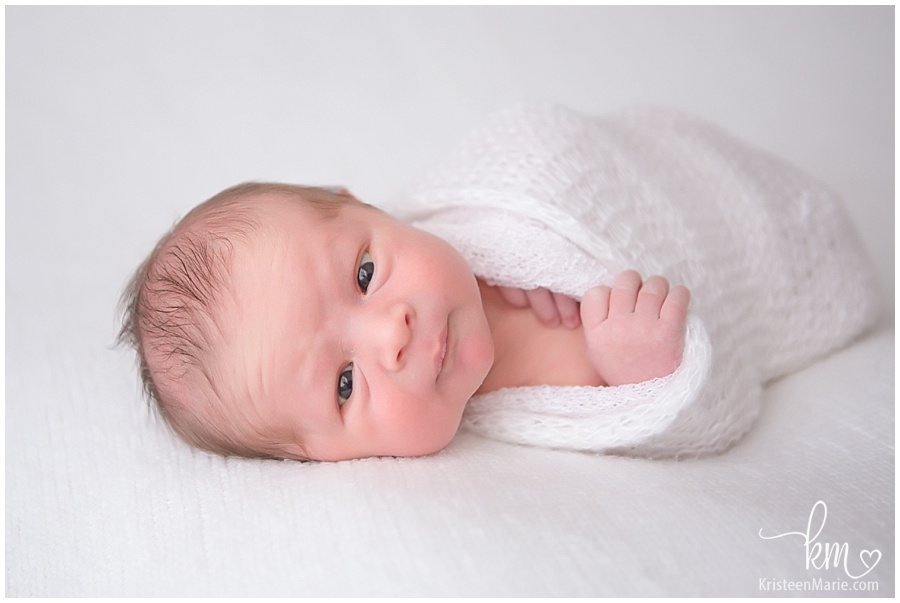 newborn baby boy with eyes open/ baby boy wrapped in white blanket