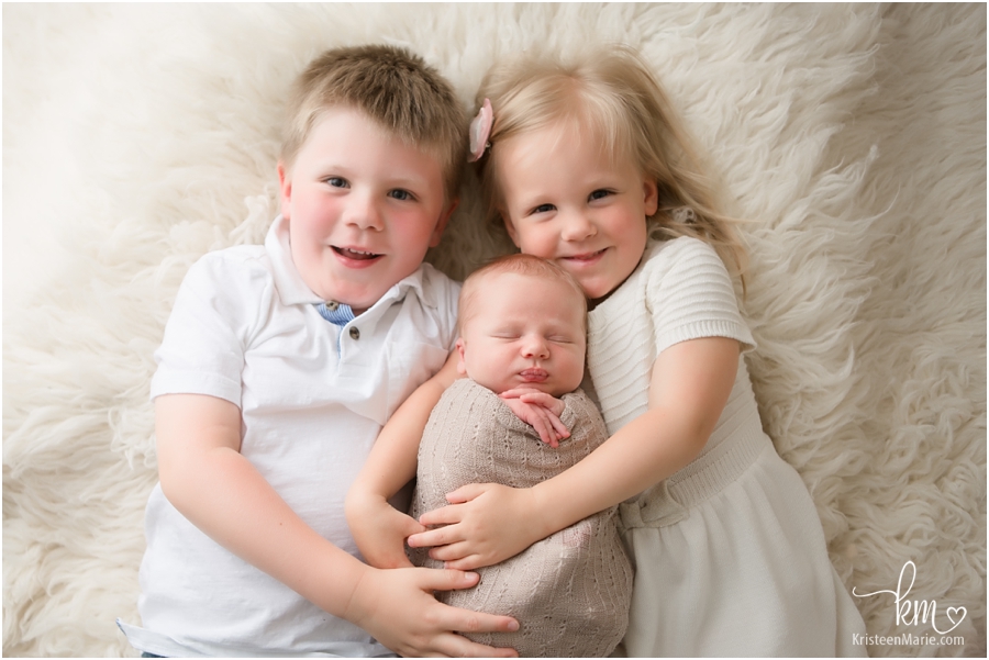 siblings laying down with newborn baby - 3 kids