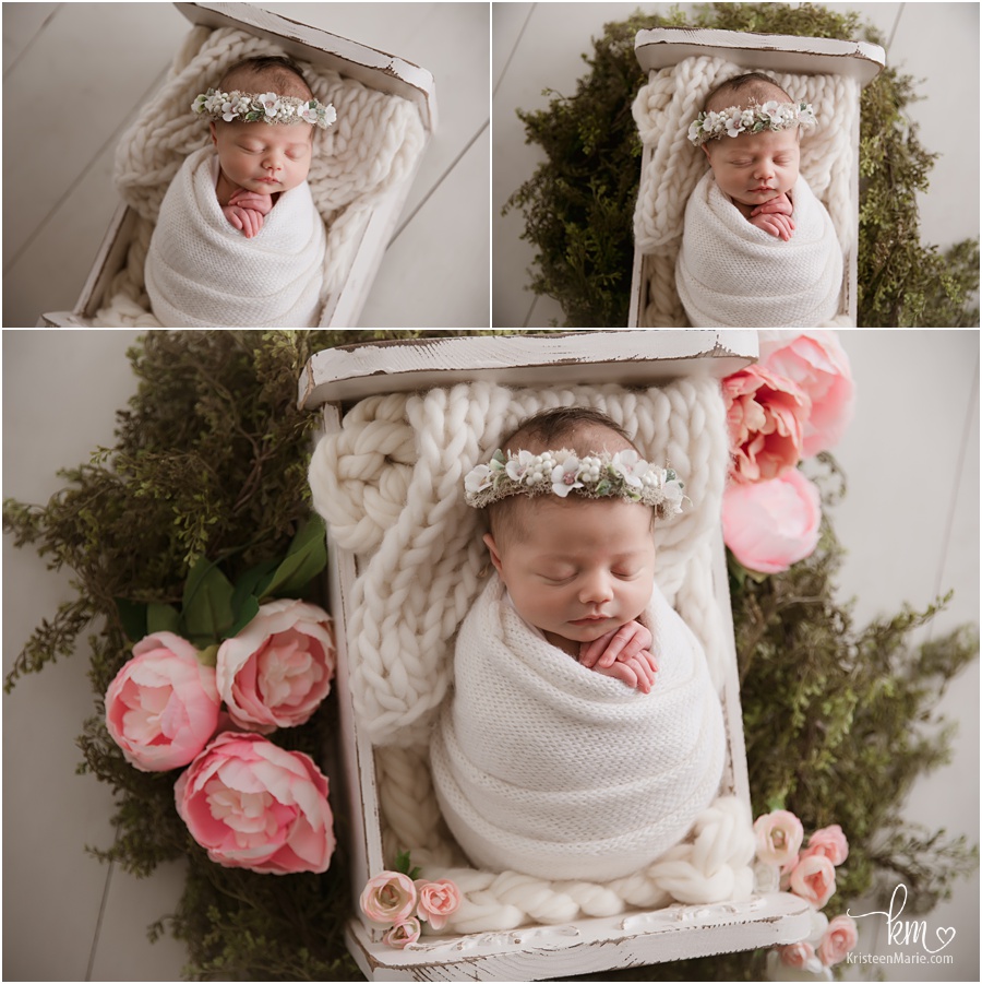 newborn baby in white whith greenery and flowers