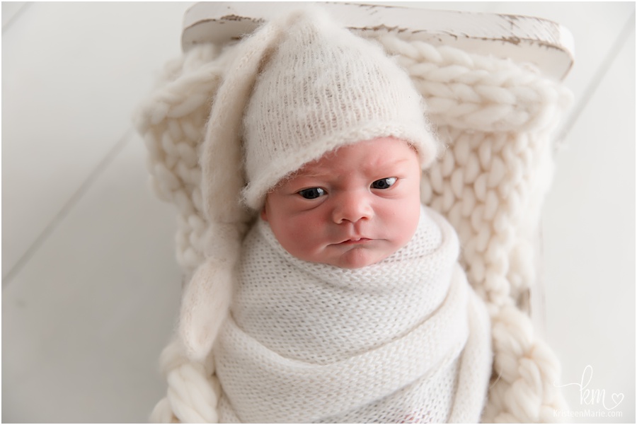 awake newborn boy in cream with hat