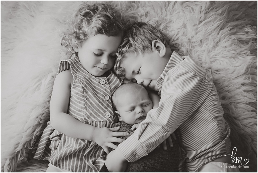 siblings cuddling newborn brother