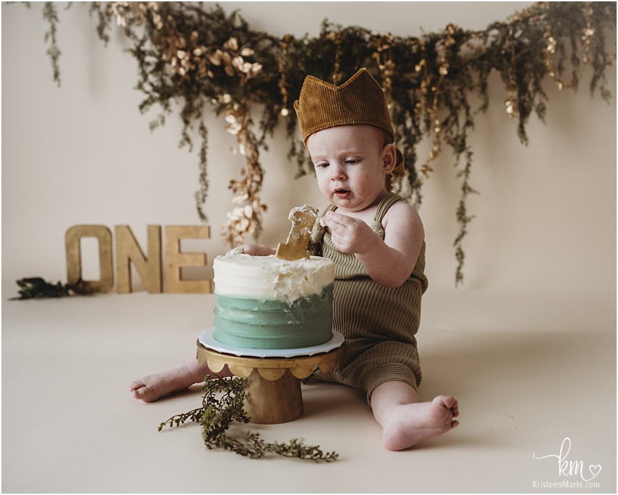 boy in crown with greenery backdrop 1st birthday cake smash photography