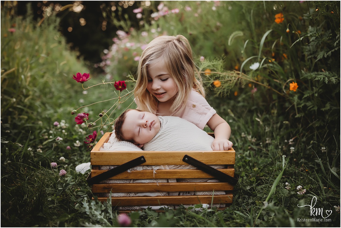 baby in wild flower field with sister - outdoor newborn photography in Indinanapolis