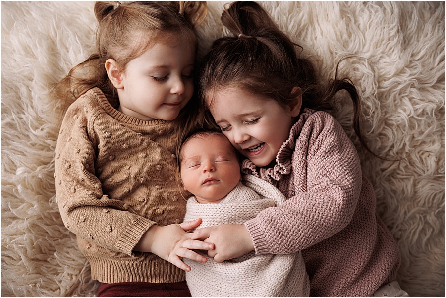 big sisters cuddling newborn baby boy