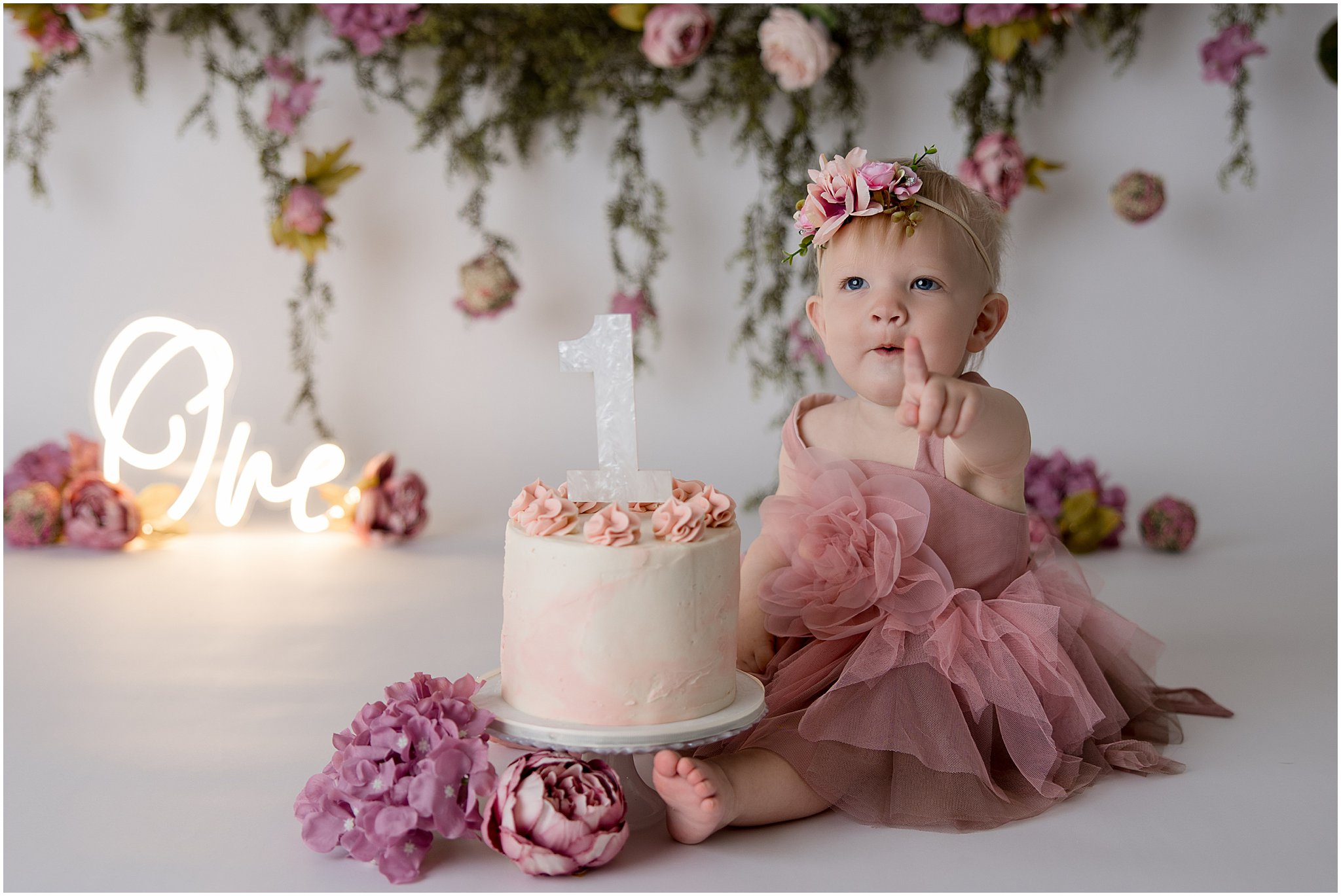 Baby girl in pink dress sitting next to cake during Zionsville cake smash session