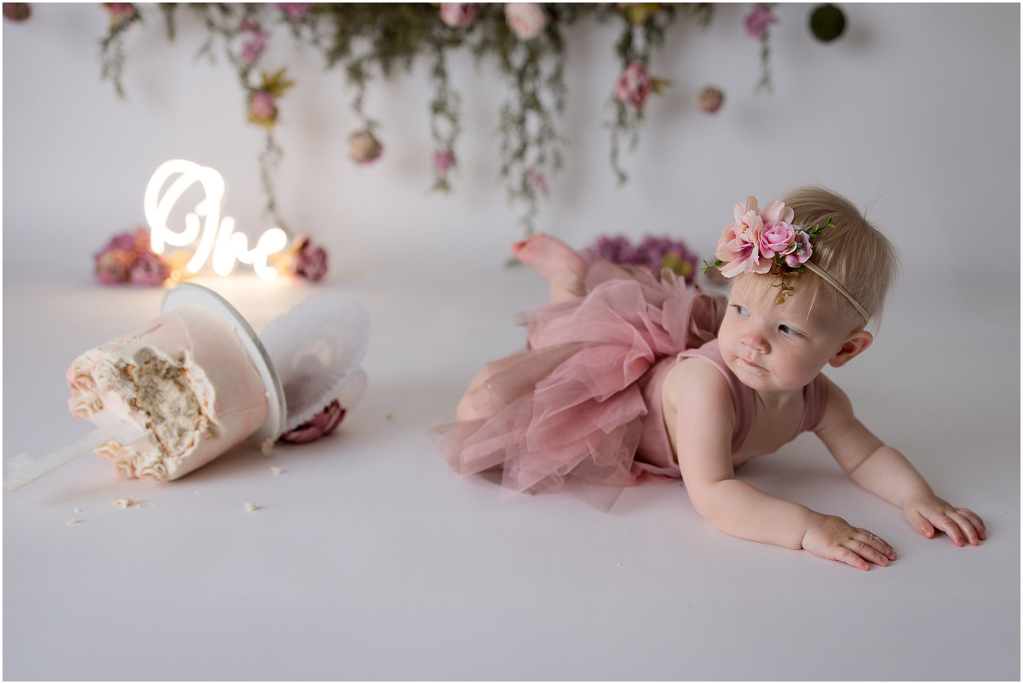 1st birthday smash cake tipped over with birthday baby looking at it - Zionsville 1st birthday cake smash photography