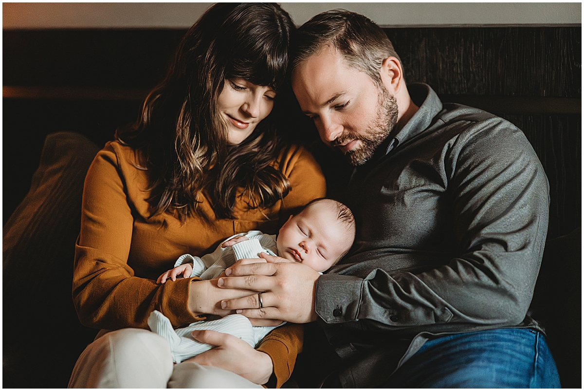 parents cuddled on bed with newborn baby