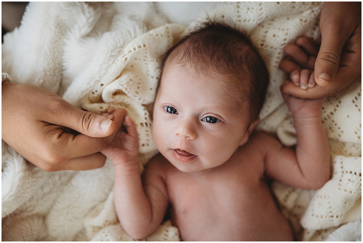 In-home lifestyle newborn photography - awake newborn girl holding mom's hands on neutral textures