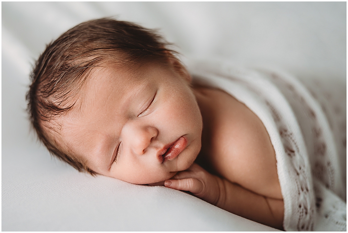 Sleeping newborn posed on a soft white surface during a Fishers newborn photography session, captured with natural tones and gentle light.
