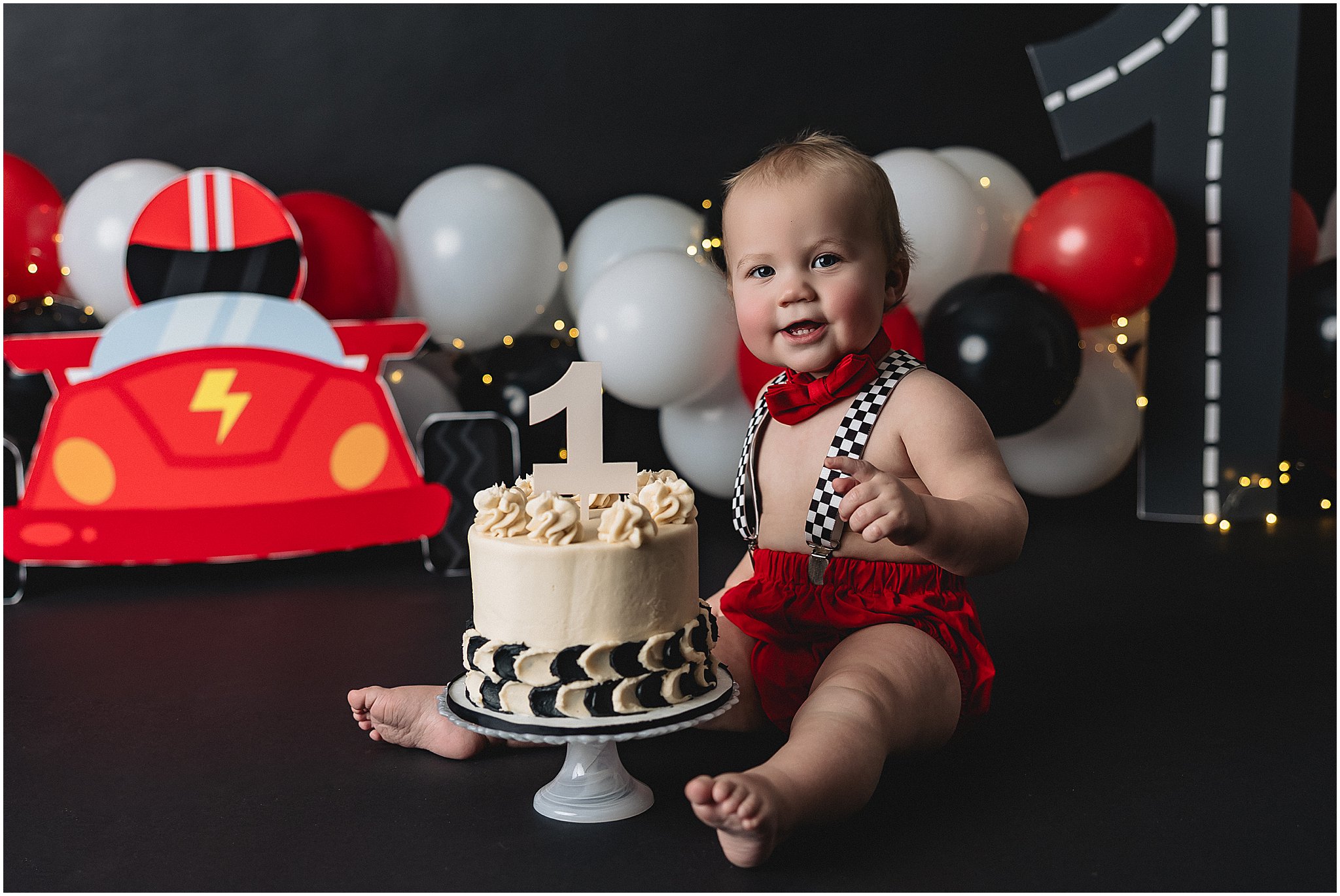 One year old boy at car themed cake smash with red and black balloons in Indianapolis photography studio