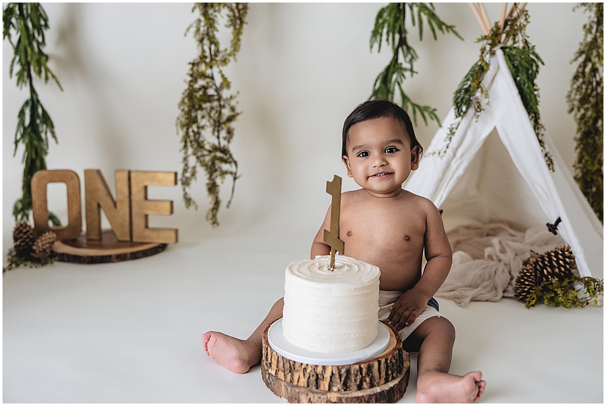 Smiling one year old boy sitting beside cake during Indianapolis first birthday photos
