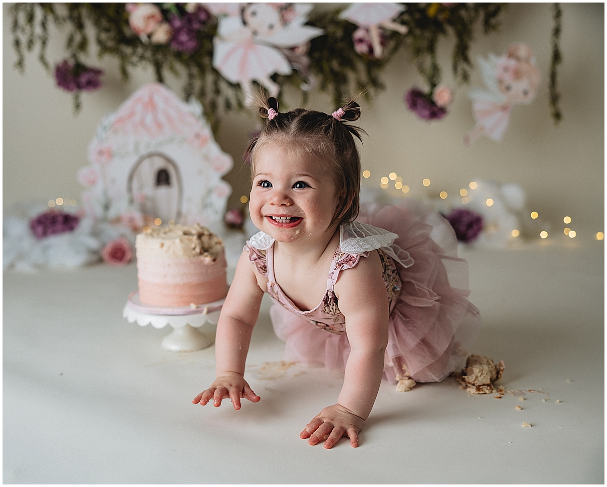 Indianapolis photographer cake smash session with baby girl crawling and smiling by birthday cake