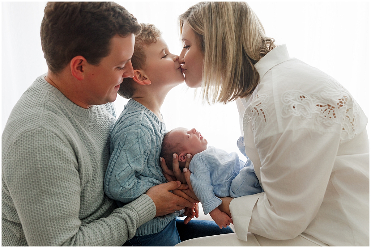 Family kissing toddler brother while holding newborn baby boy during lifestyle newborn photography session in Indianapolis