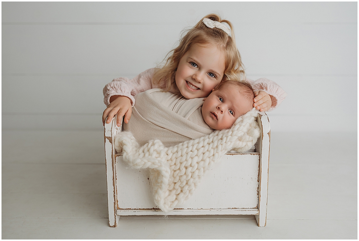 Sibling newborn portrait with toddler sister and baby wrapped in neutral studio setup