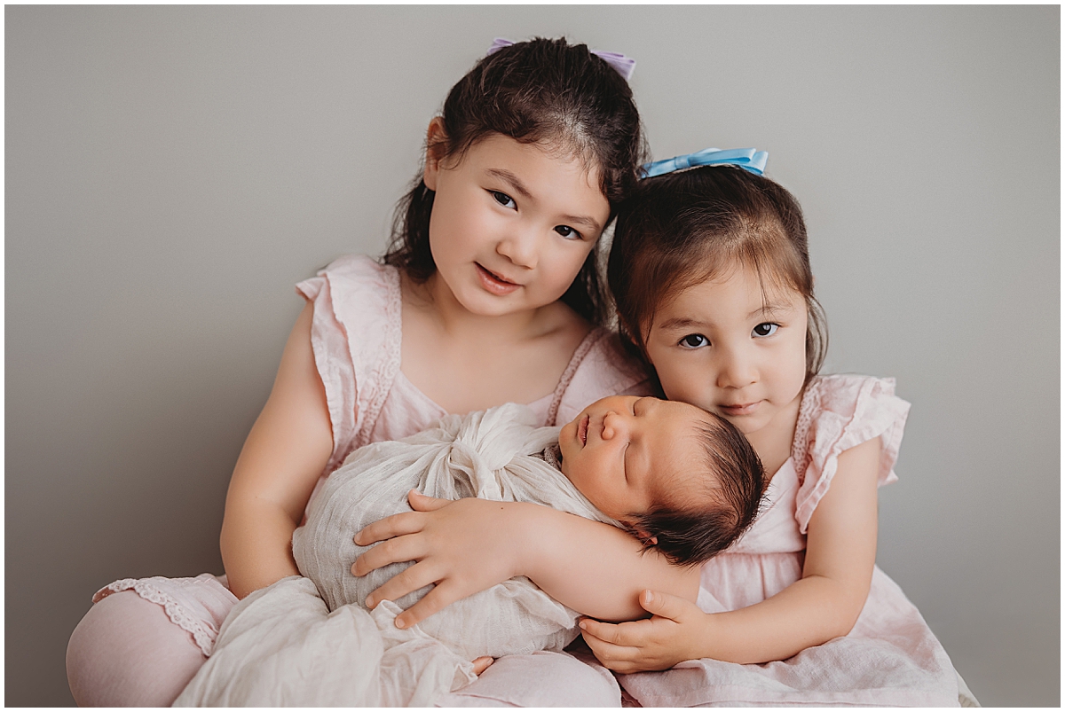 Big sisters smiling with their newborn baby brother during Indianapolis newborn photography session