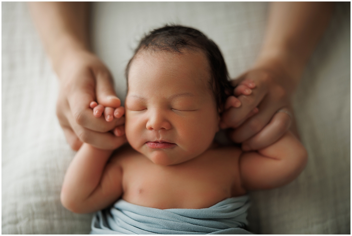 Close-up newborn portrait of baby boy sleeping with soft blue newborn photography styling - holding mom's hands