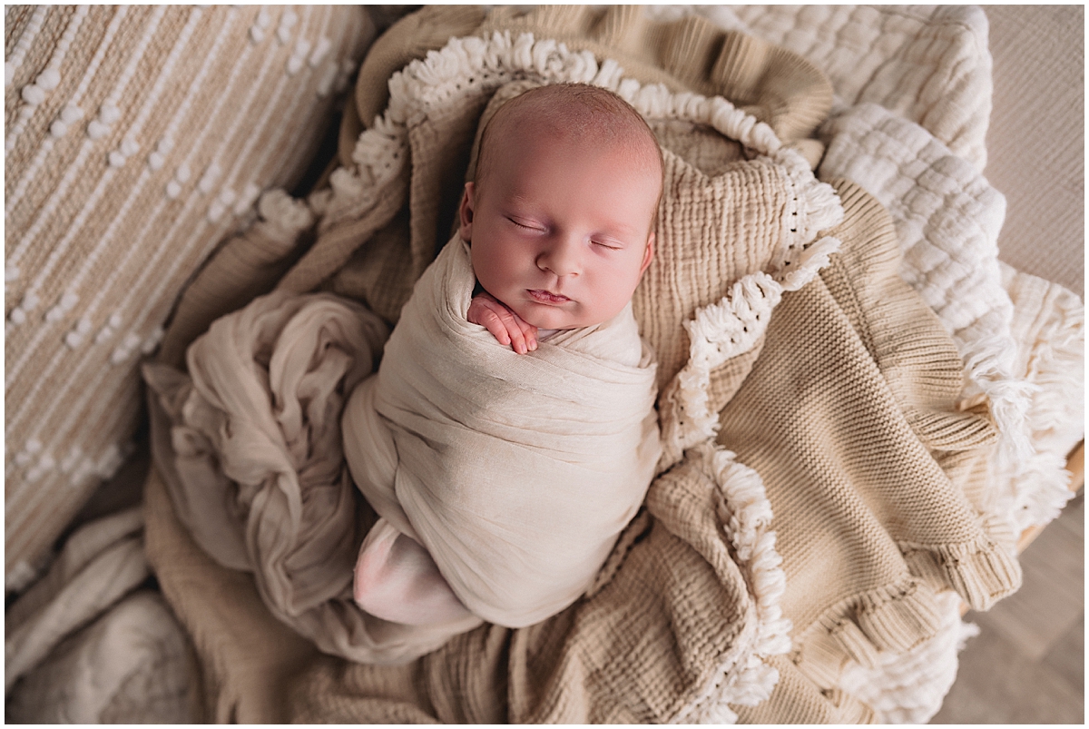 sleeping newborn looking at the camera while wrapped in a green swaddle