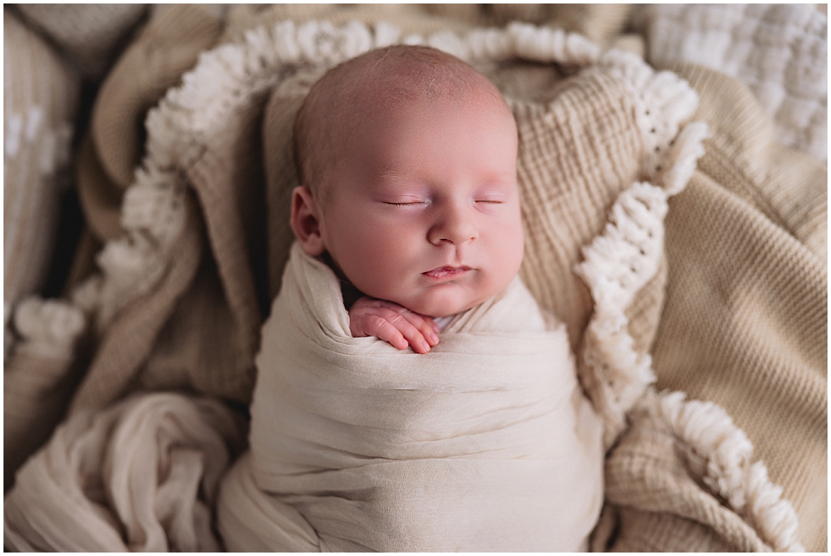 Sleeping newborn wrapped in cream and surrounded by neutral textured blankets