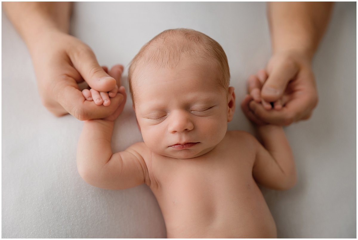 Close-up of parents holding their sleeping newborn baby’s hands during a studio session.