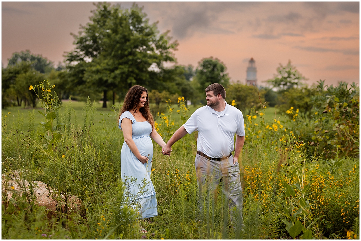 Expecting couple holding hands in a summer wildflower field at Coxhall Gardens in Carmel, Indiana.