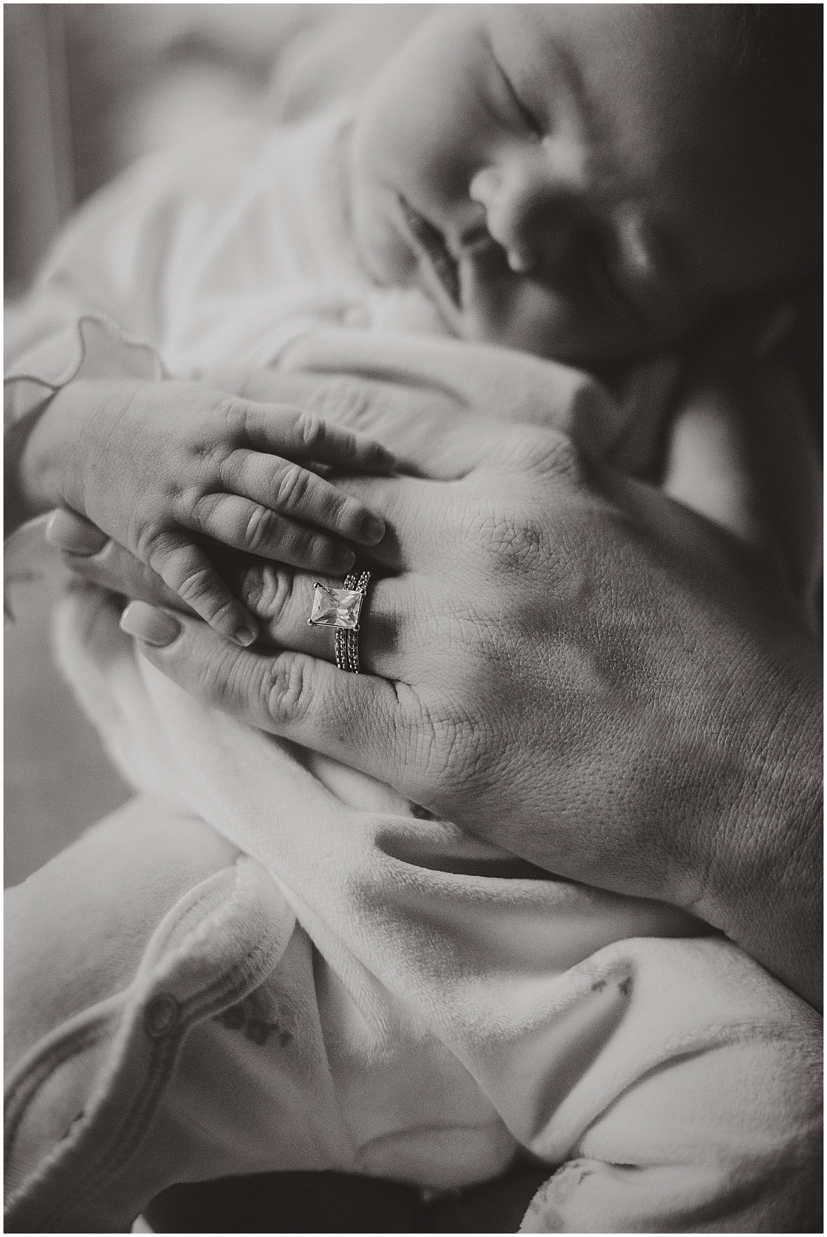 Black-and-white close-up of parents’ hands resting gently on their newborn.