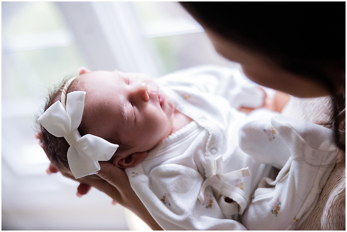 Sleeping newborn girl in a white wrap on a pink-and-green quilt.