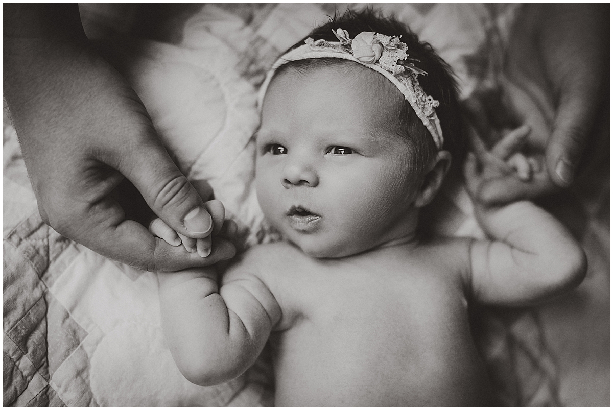 1003 Newborn girl holds a parent’s finger in a black-and-white portrait.