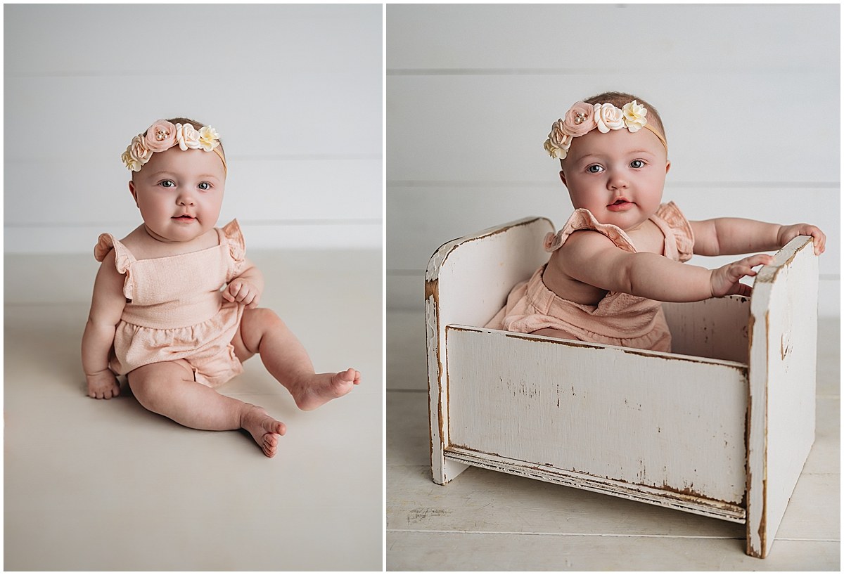 Baby sitting independently in a peach outfit, paired with a portrait in a small wooden prop bed.