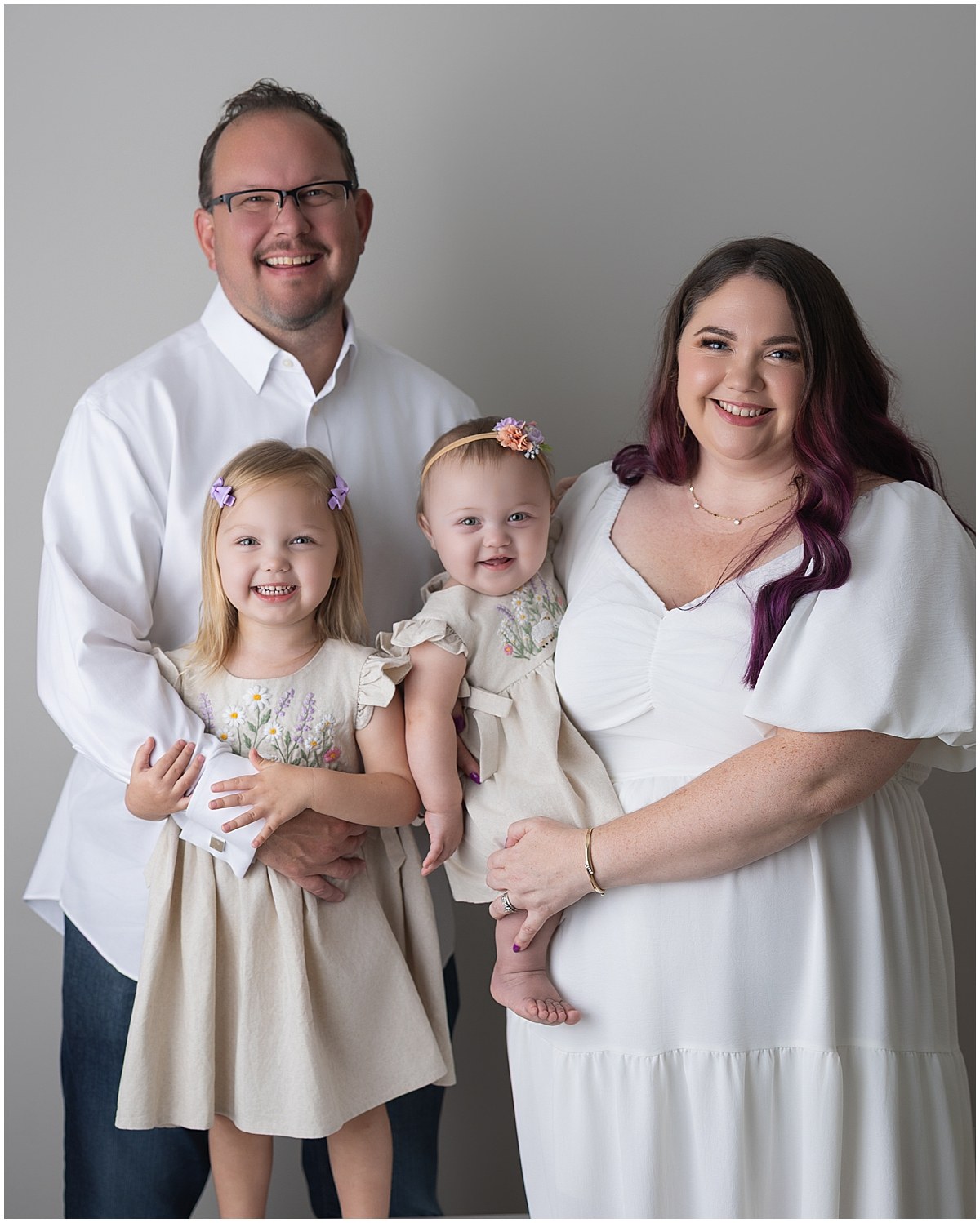 Parents with their two daughters in coordinating cream outfits for first birthday family pictures.