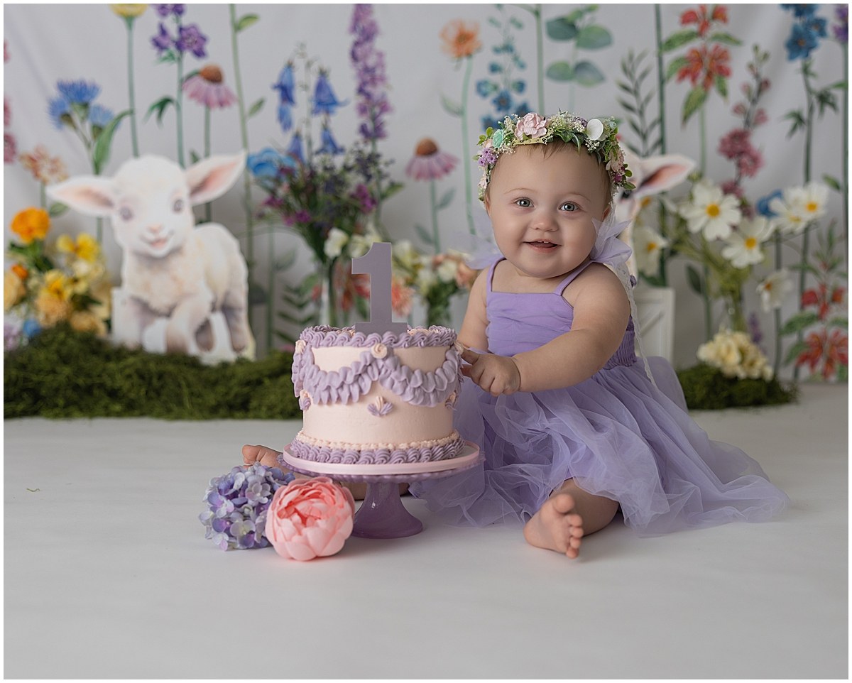 Smiling one-year-old celebrating her Grow With Me graduation with a floral cake smash setup.