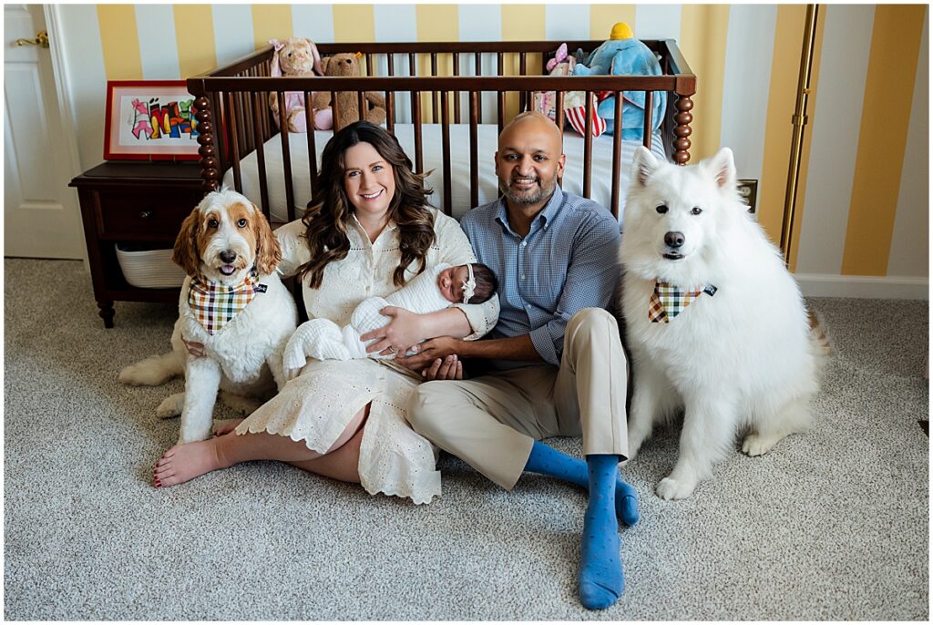 Parents holding their newborn baby beside two family dogs in the nursery.