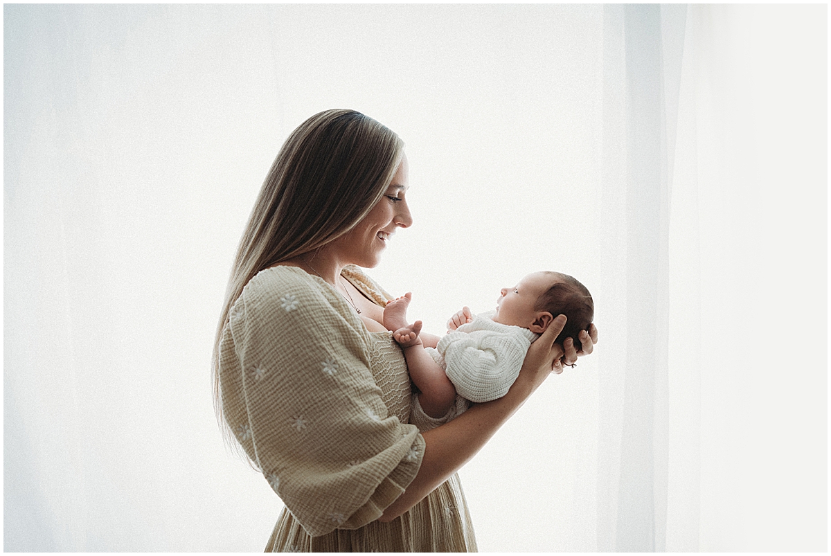 Mother holding her newborn beside a bright window during an Indianapolis newborn photography session.
