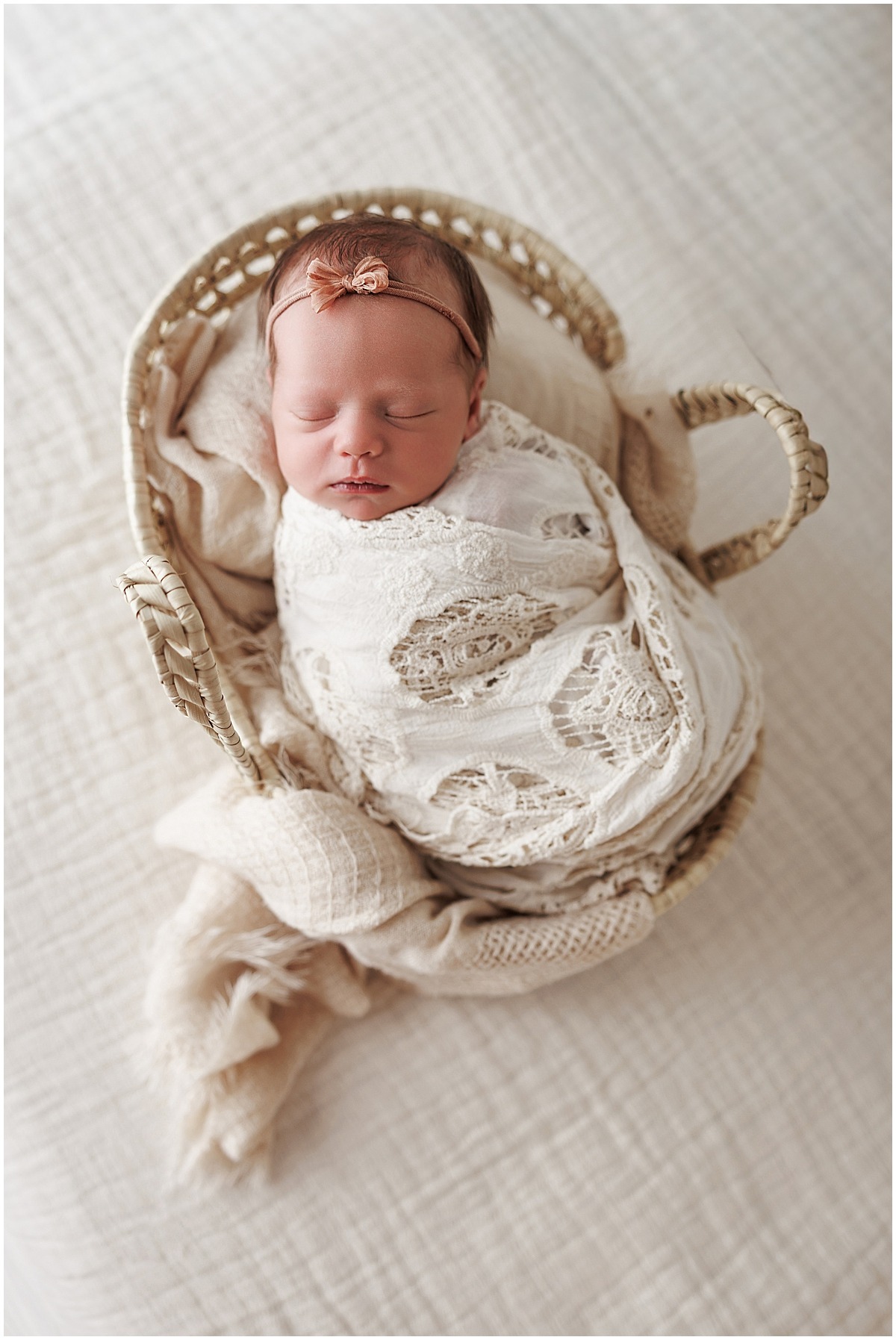 Sleeping newborn girl wrapped in cream and posed in a woven basket during an Indianapolis newborn session.