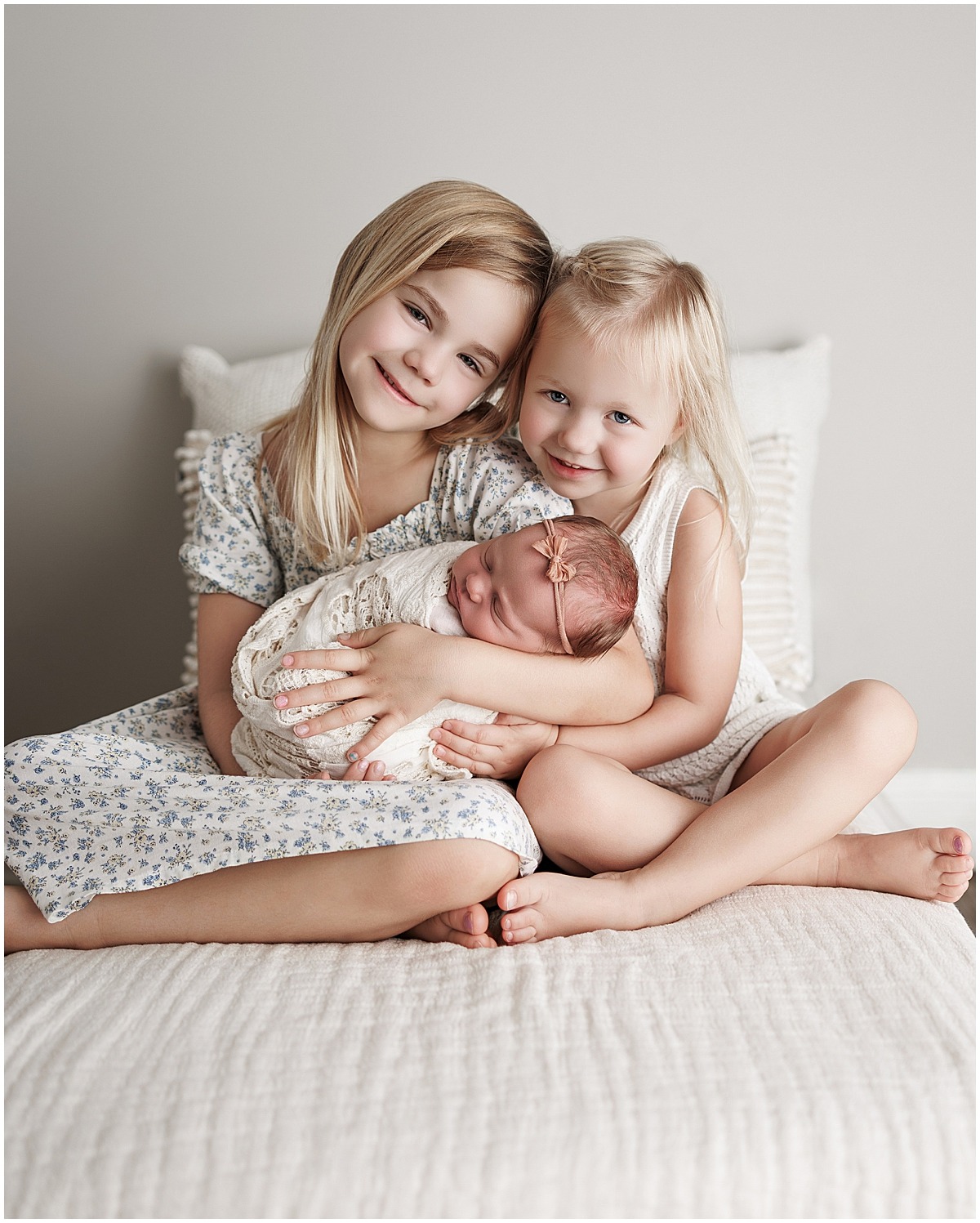 Two smiling older sisters hold their sleeping newborn sister during an Indianapolis studio session.