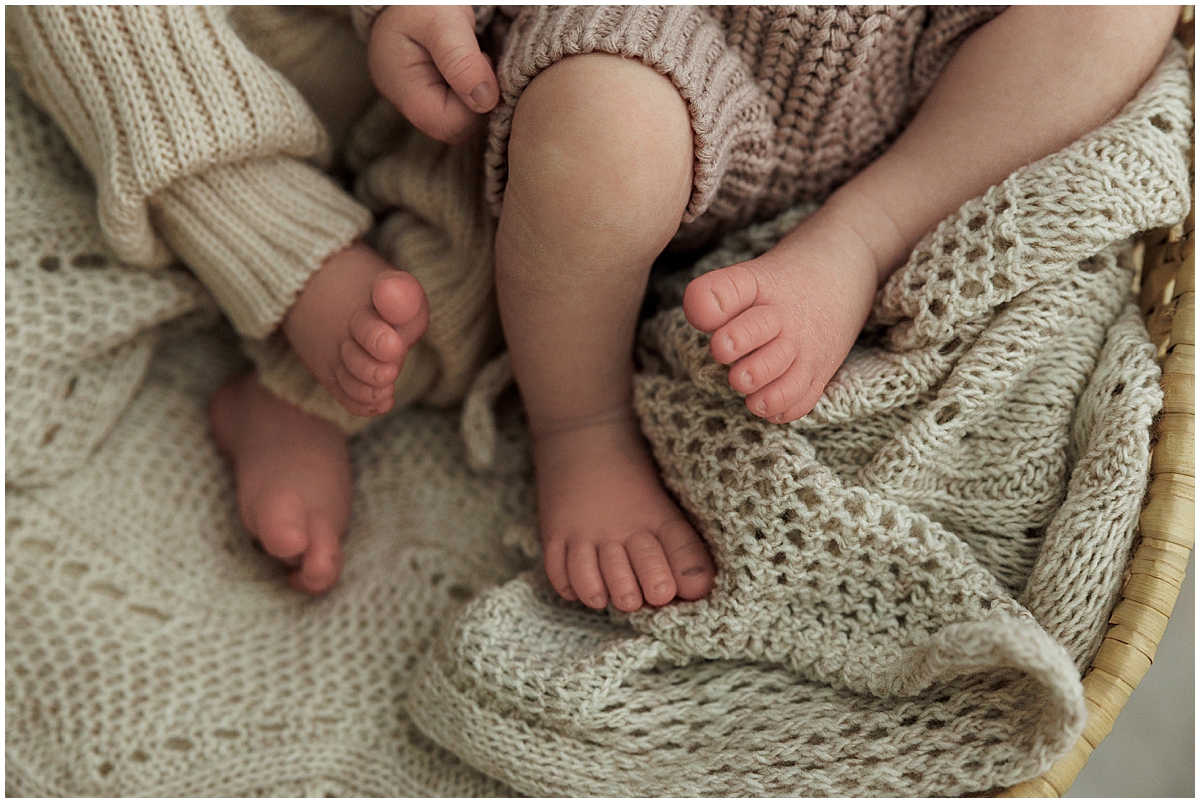 Close-up of both twins’ tiny feet resting together on a textured cream knit blanket.