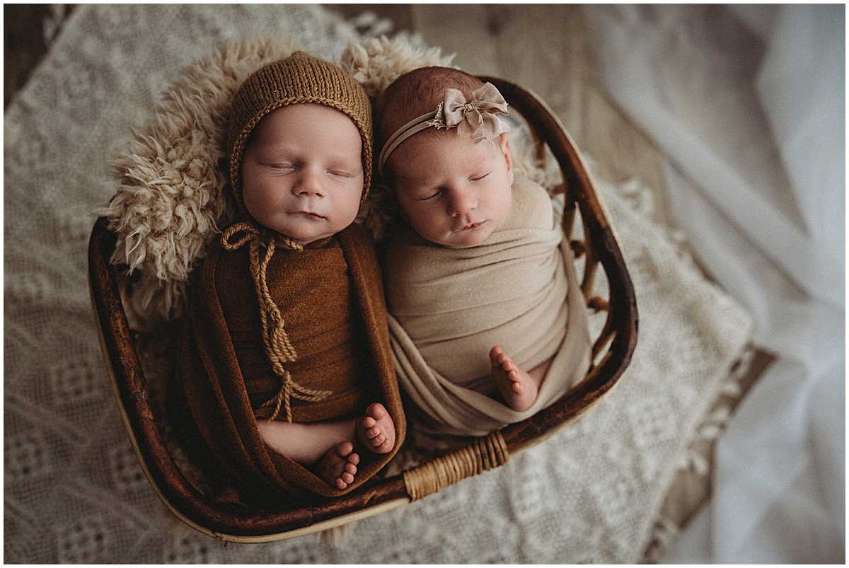 Overhead portrait of wrapped twins nestled together in a rustic basket on cream blankets.
