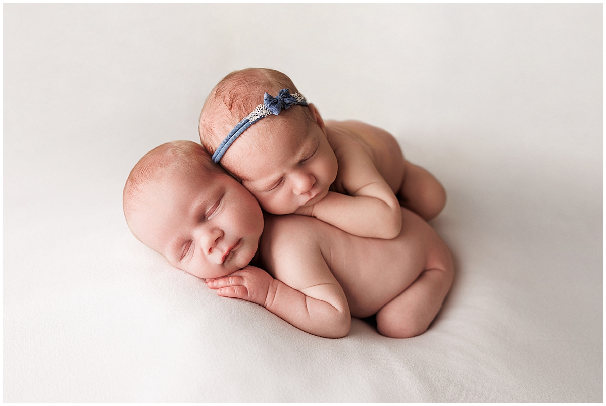 Newborn twins sleeping nestled together on a cream backdrop.