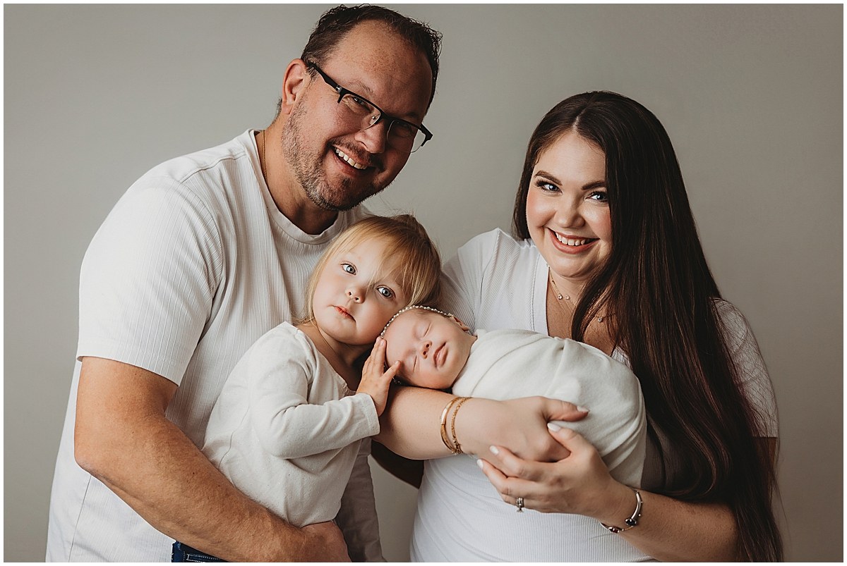 Parents and older sister cuddling a wrapped newborn during a studio family portrait.
