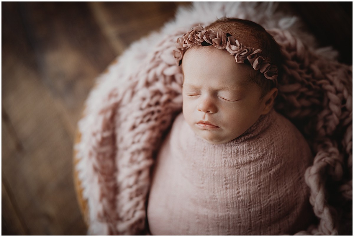 Sleeping newborn wrapped in mauve with a floral headband and textured blanket.