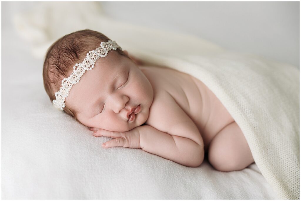 Sleeping newborn baby wearing a delicate headband on a simple light studio backdrop.