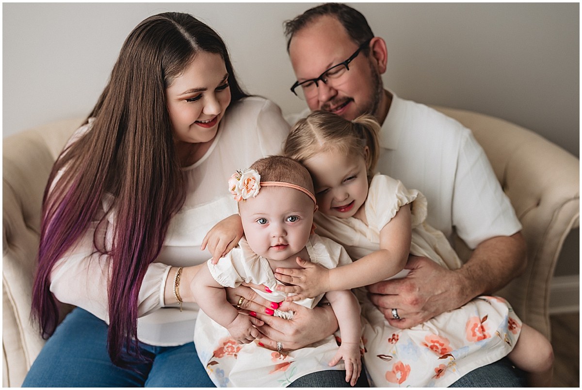Parents sitting on a couch with their baby and older daughter during a sitter milestone session.