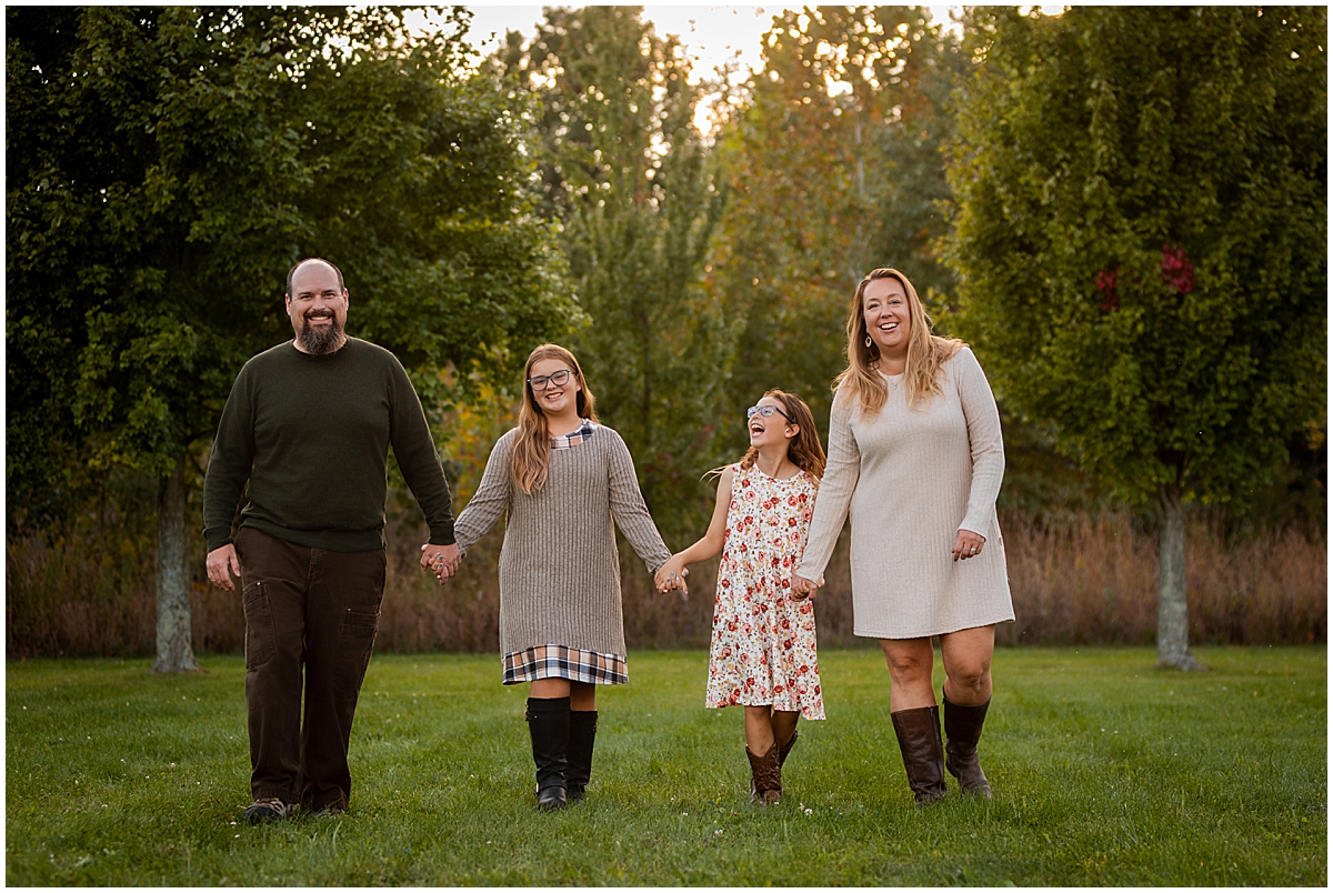 Parents and their two daughters walk hand in hand across a grassy lawn.