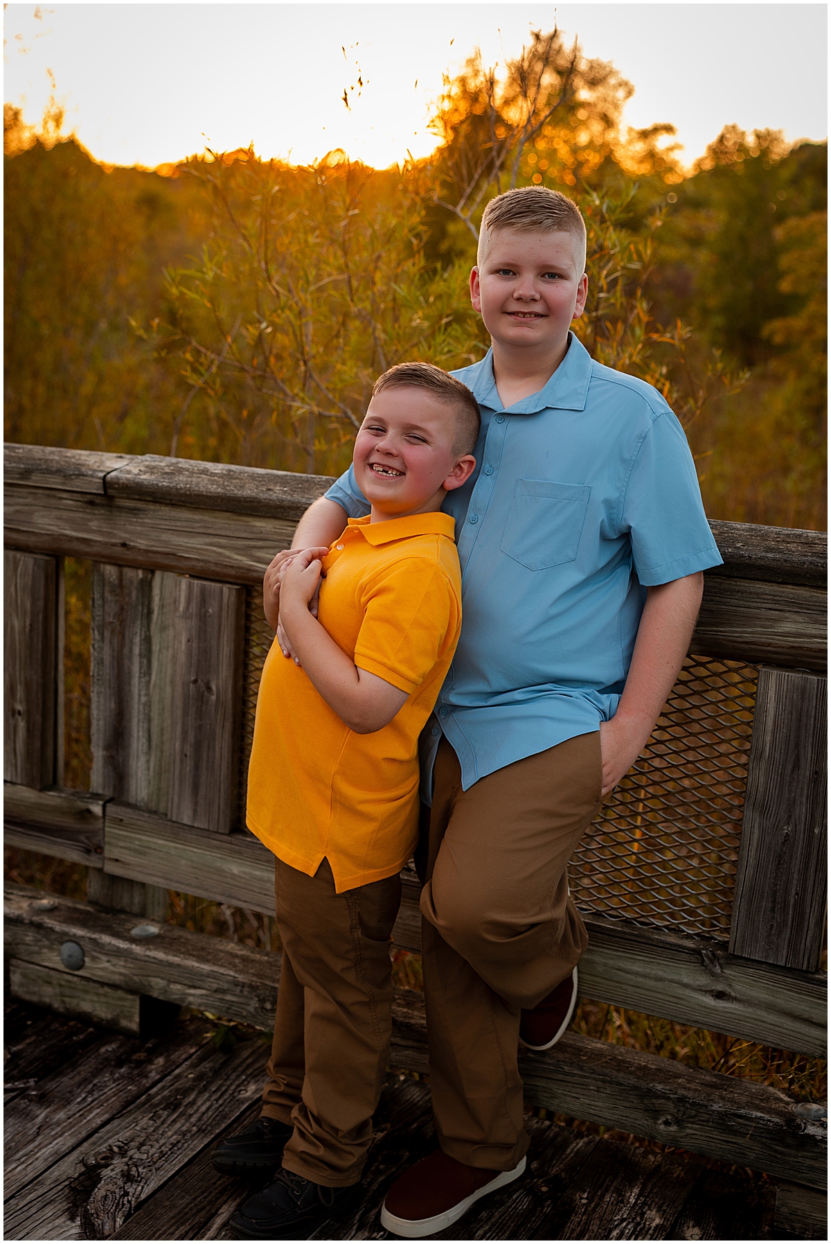 Two brothers hug beside a wooden railing at sunset.