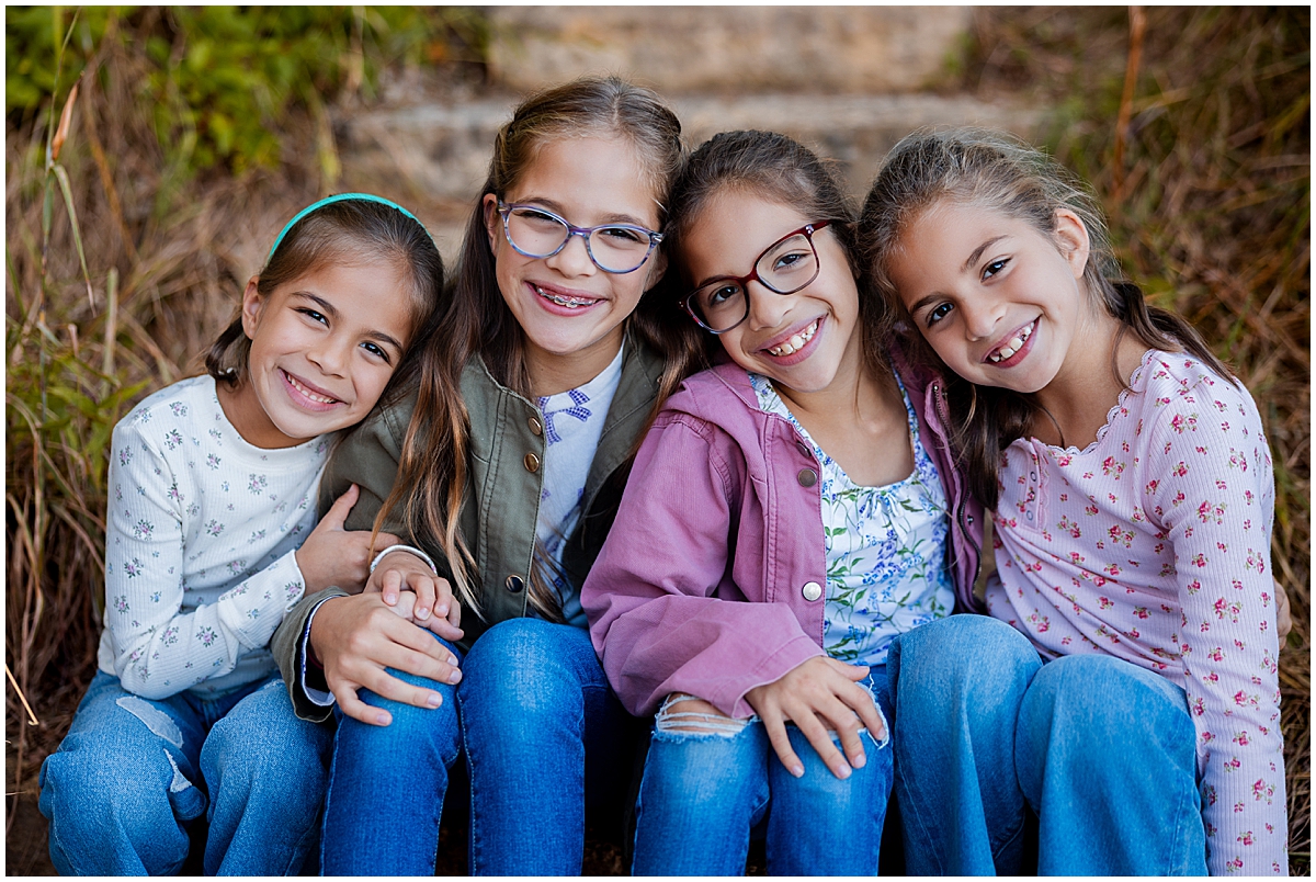Four sisters lean together and smile while sitting on outdoor steps.