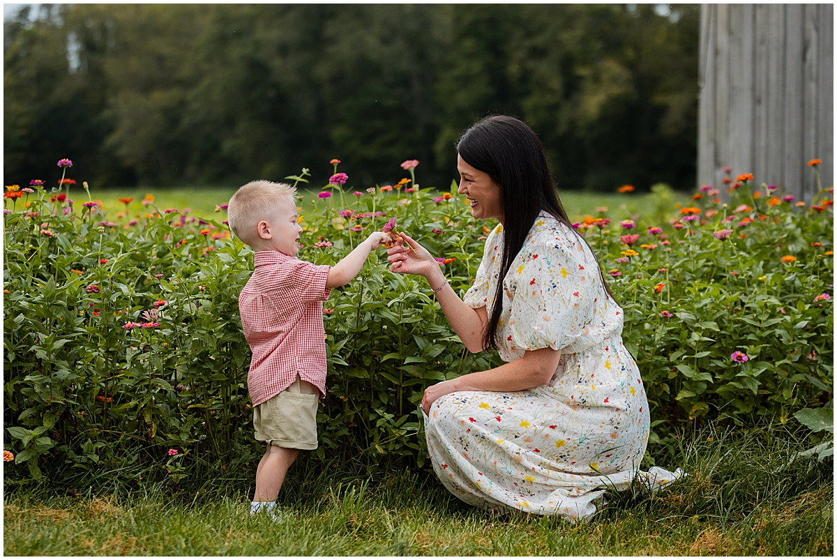 Mother kneeling beside her son as they hold flowers together beside the field.