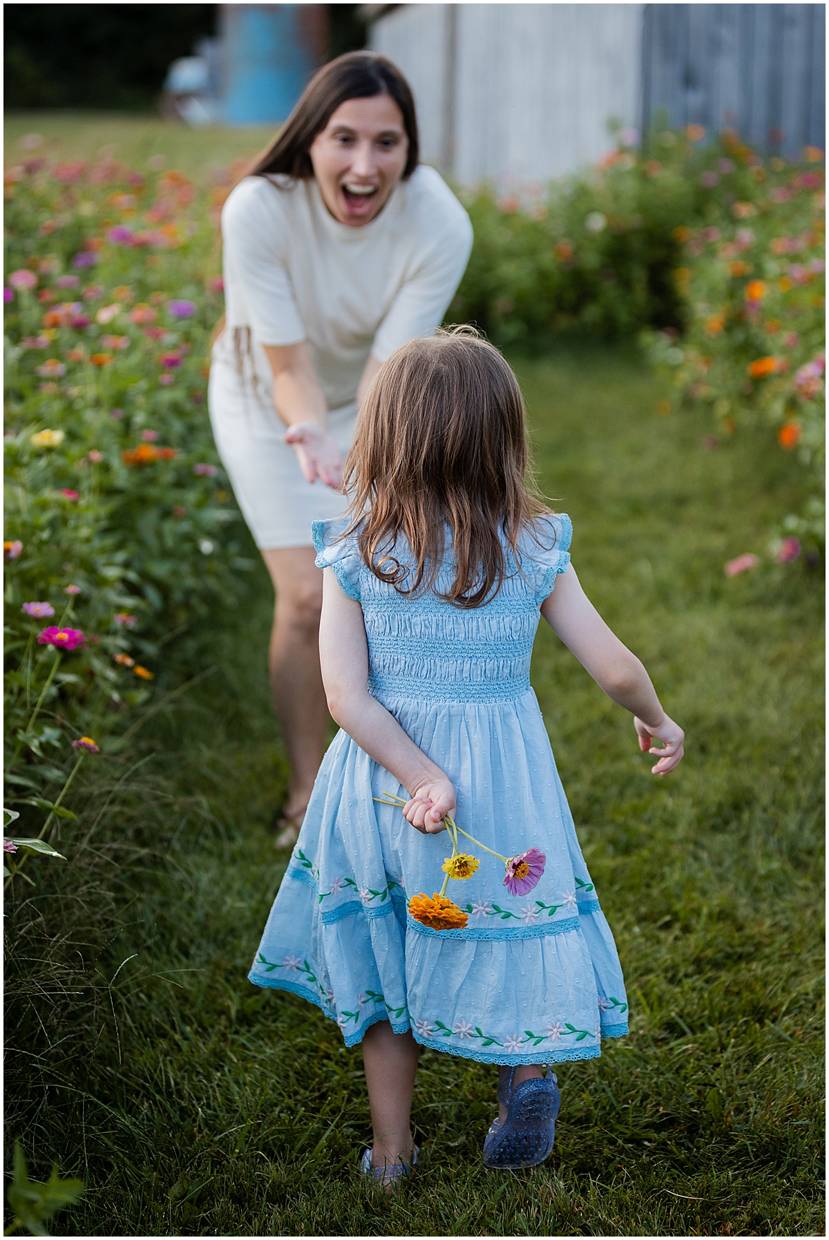 Girl holding a small bouquet behind her back as she approaches her smiling mother.