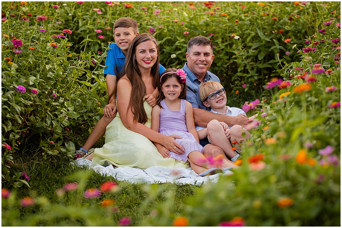 Family of five cuddling on a white blanket framed by colorful wildflowers.