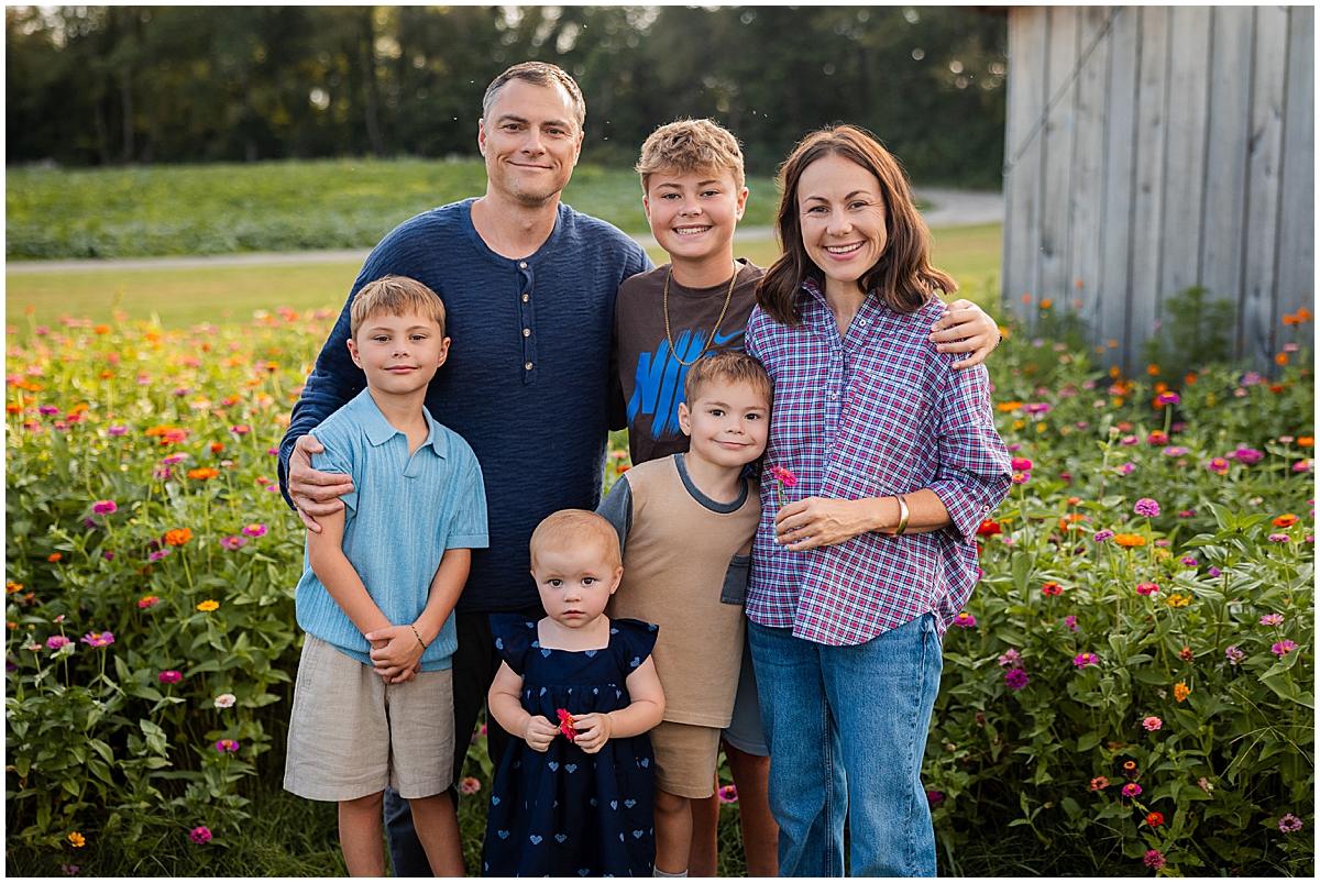 Family of six standing together beside the colorful flower field and weathered barn.